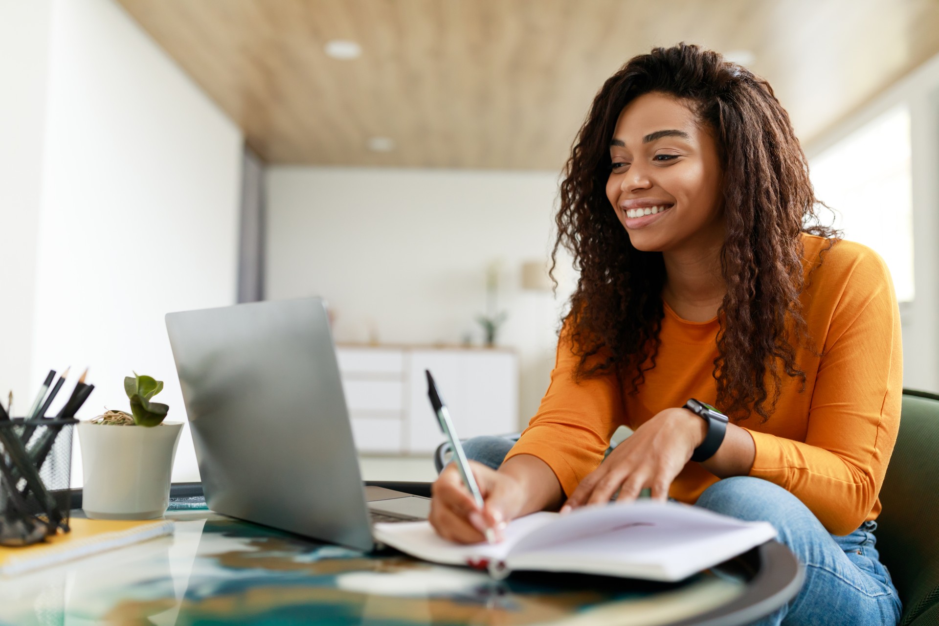 Black woman sitting at desk, using computer writing in notebook Black woman sitting at desk, using computer writing in notebook